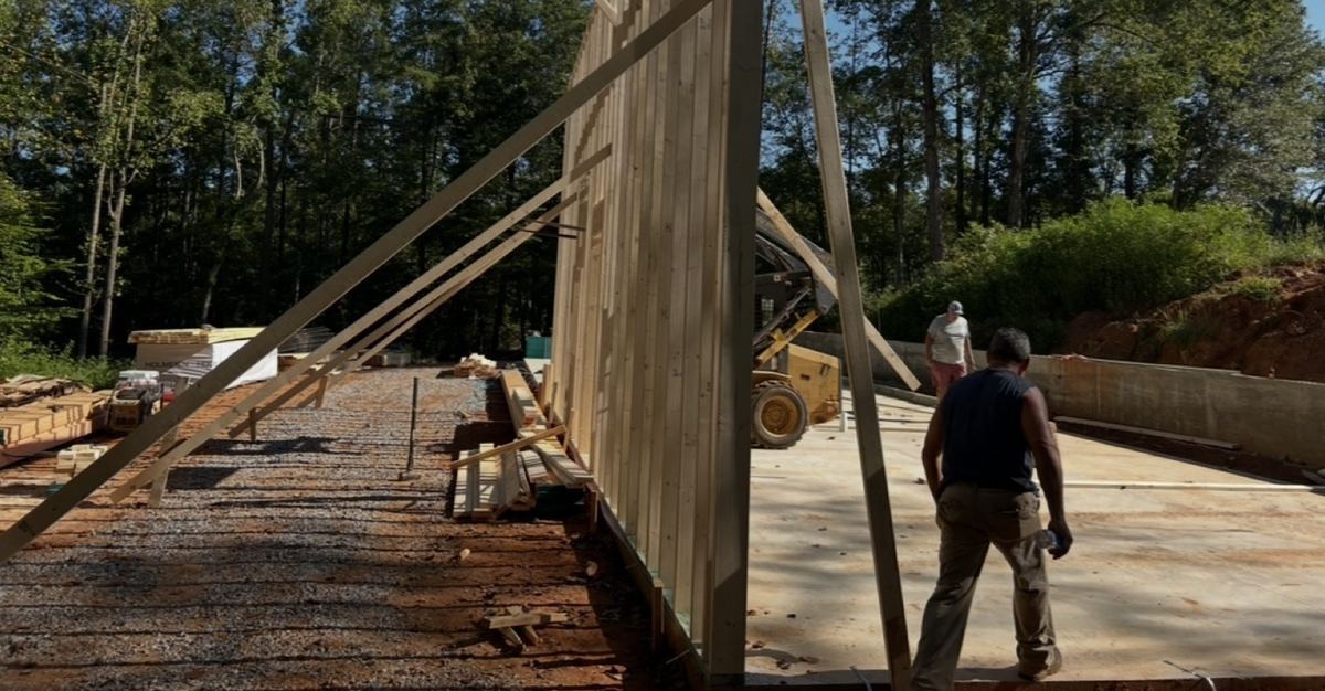 Wall framing raised on a finished concrete slab next to a concrete wall